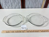 Two clear glass pie dishes on table with ruler for scale