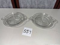 Two clear Manhattan pattern plates with handles on tabletop, lot number visible