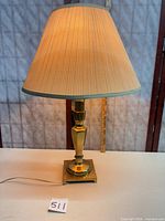 Full view of brass lamp with shade illuminated, showing base design and pleated shade