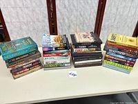 Three stacks of assorted hardcover and paperback books on table