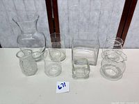 Eight assorted clear glass vases displayed on tabletop