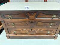 Front view showing three drawers, brass ring pulls, carved motifs