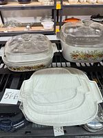Two square CorningWare casseroles with glass lids, three plastic lids stacked in front