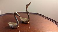 Front view of both brass swans on wood surface