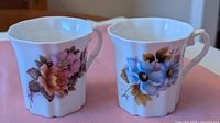 Two mugs showing orange-pink roses and blue flowers