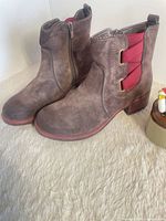 Full view of both boots showing suede texture, red elastic detail, stacked heel