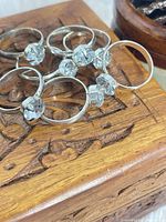 Group of seven matching silver-tone rings with clear stones on carved wood box