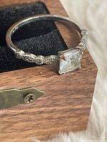 Side view of ring on wooden box showing band pattern and stone