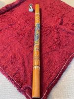 Full view of bamboo didgeridoo on red fabric showing length and painted section