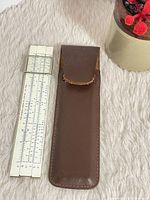 Slide rule alongside leather sleeve on fabric background