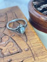 Ring on wood surface showing overall design and central opalescent stone with two clear accent stones