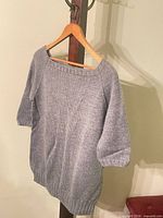 Full view of light grey hand knit sweater on hanger