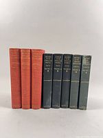 Front view of seven books: three red cloth volumes and four dark green volumes