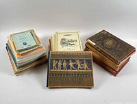 Three distinct piles: stack of softcover booklets, Schubert Album cover visible, hardbound Meister Lieder and ornate brown hardbound volume