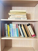 Full shelf view showing horizontal stack of books on upper shelf and standing volumes on lower shelf