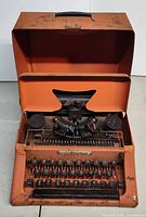 Front view of open Tom Thumb orange toy typewriter showing keys and mechanism