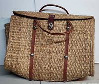 Front view of woven straw handbag showing leather handle, strap, accents and clasp