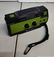 Front view showing brand, speaker grille, controls, strap