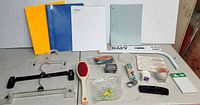 Overall view of folders, writing pad, green sheet, hangers, hairbrush, pencils, labels, bumper sticker, metal bar and small accessories