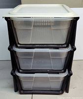 Front view of three clear bins stacked in black frame with white lid on top