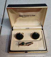 Open box showing cufflinks and tie clip