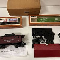 Overview showing two boxed Tyco boxcars, Lionel caboose with sheet, black building parts, plain carton