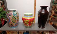 Front view of three ceramic vases on shelf with ruler for scale