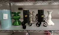Full set on shelf: blue candle, green glass holder, silver glass holder, two black candles on wrought iron stands, white ceramic holder