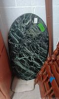 Full view of the oval green marble table top leaning against wall