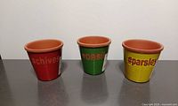 Three colored terracotta herb planters labeled #chives #basil #parsley