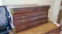 Front view of wooden campaign chest showing three drawers and brass corner protectors