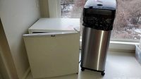 Avanti compact fridge next to stainless steel touchless trash can in window alcove