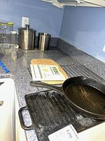 All items on countertop including cast iron pans, stainless canisters, glass loaf dish, cooling racks, cutting board, dishcloth pack, plastic pitcher