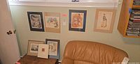 Overall view of six framed works on wall and two leaning against wall in sitting area