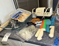 Overview of countertop with sharpener, knives, cutters, baking dish, measuring cups, aluminum pans