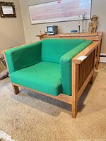 Front three-quarter view of the oak armchair showing green upholstery and slatted oak sides