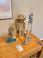 Lot overview showing both child figurines, Galileo thermometer, silver bud vase with stems, and art glass centerpiece on wooden surface