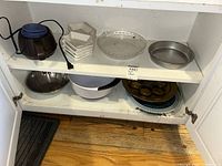 Cabinet shelf showing electric warmer, stack of condiment dishes, glass pie plate, metal cake pan, mixing bowls