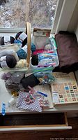 Overall view of yarns in basket, plastic bins, fabrics and pattern books on table
