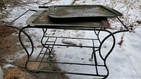 full view of green metal bar cart with two trays stacked on top, showing frame, lower shelf and casters in outdoor snow setting