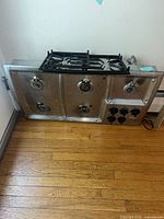 Front view of stainless steel 5-burner cooktop with control knobs and cast iron grates