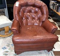 Front view of brown leather tufted club armchair showing overall design and wear
