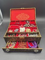 Open jewelry box showing exterior pattern, red velvet interior, trays, drawer, and assorted jewellery