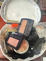 Open bag showing Maybelline blush compacts, sealed compact, pencils and other items