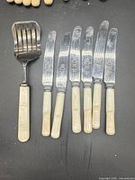 Full set of six knives and slotted server displayed on black surface