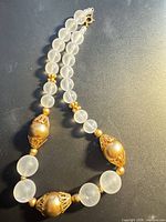 Full view of necklace laid flat showing frosted beads, gold-tone filigree beads and clasp