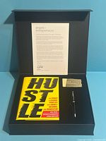 Open presentation box showing Hustle book, pen, founder card, introduction letter