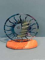 Front view of painted metal sun sculpture on sandstone base
