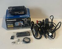 Camcorder on box with remote, lens ring, cables and charger visible