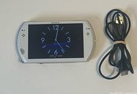Front view of white Sony PSP Go console displaying clock screen alongside USB cable